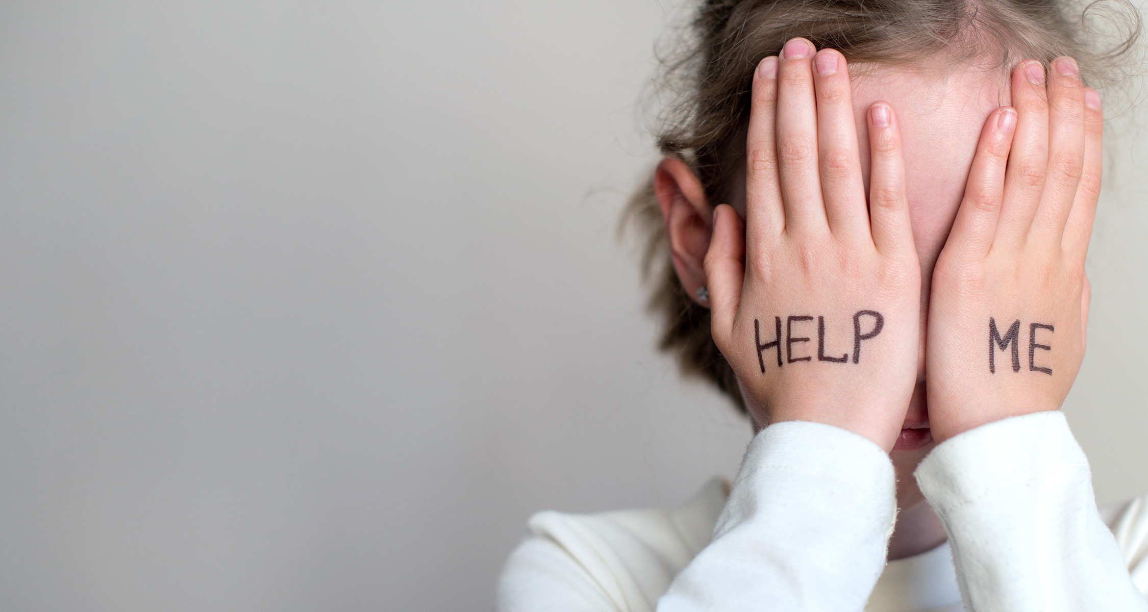 Mädchen hält sich ihre Hände vor ihr Gesicht, auf denen "Help Me" steht
